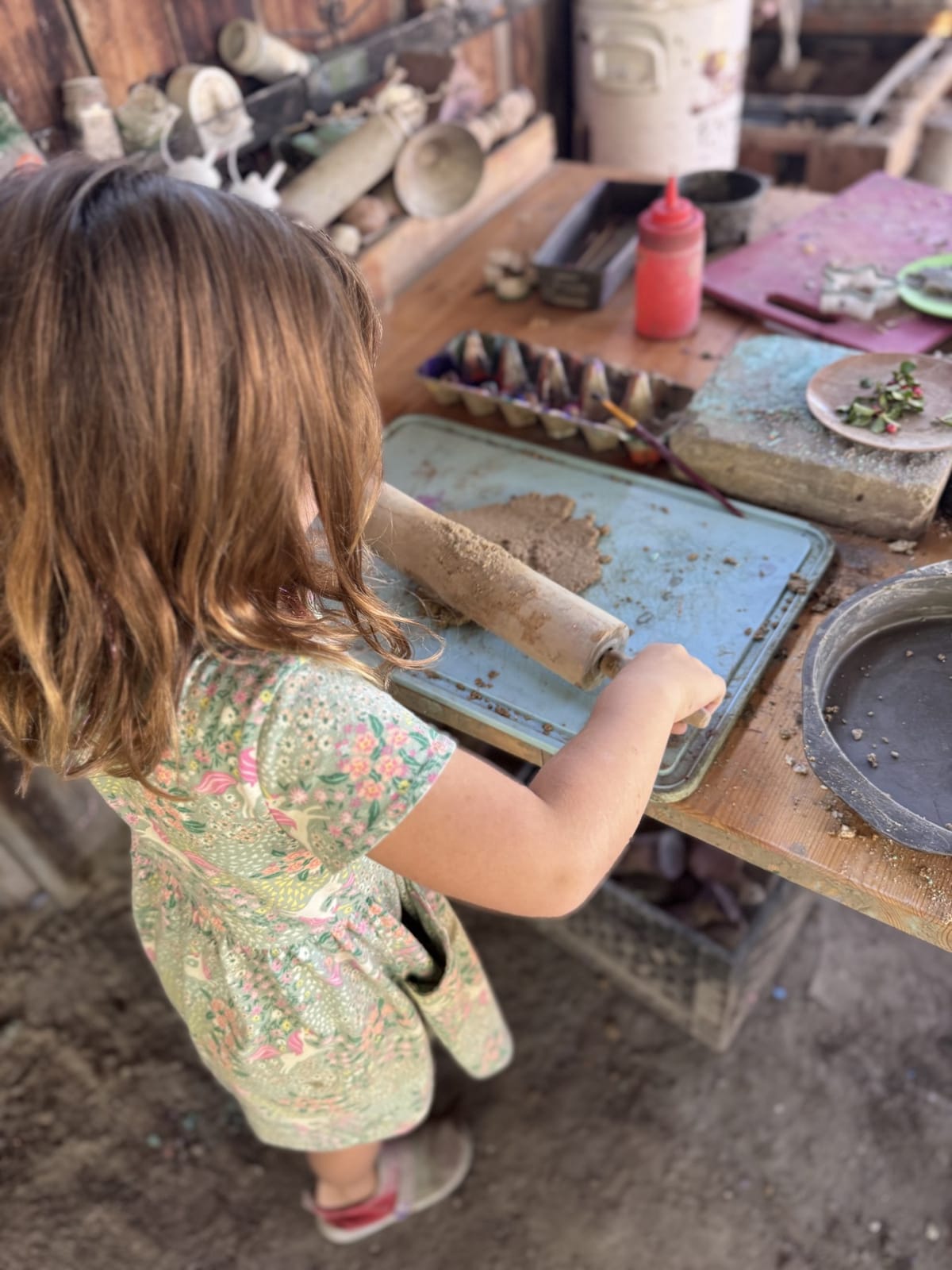 A child rolling mud with a rolling pin in the mud kitchen